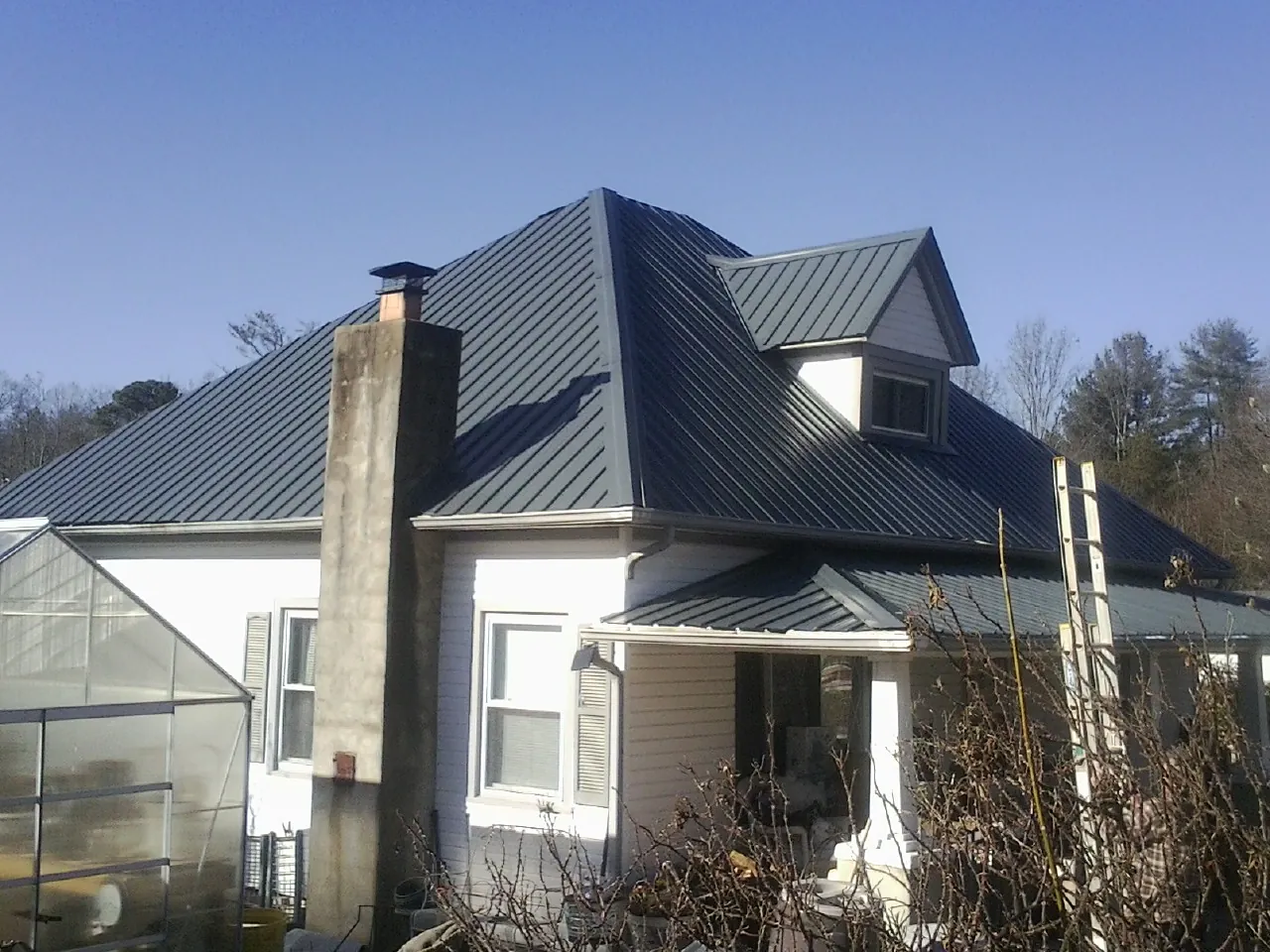 Dark blue standing seam metal roof on a white farmhouse with dormer — Slate & Tile Roof Repair by Roofing Brothers in Atwood