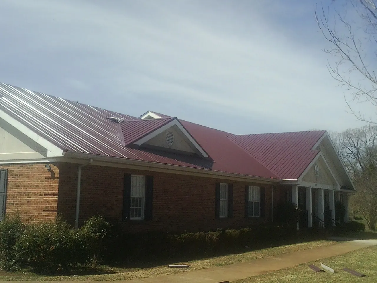 Red metal roof with gabled entries on a long brick building, from a Hail Damage Roof Repair job in Atwood