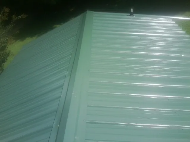 New green metal panels meeting at the ridge of a roof — Flat Roof Repair work by our crew in Atwood