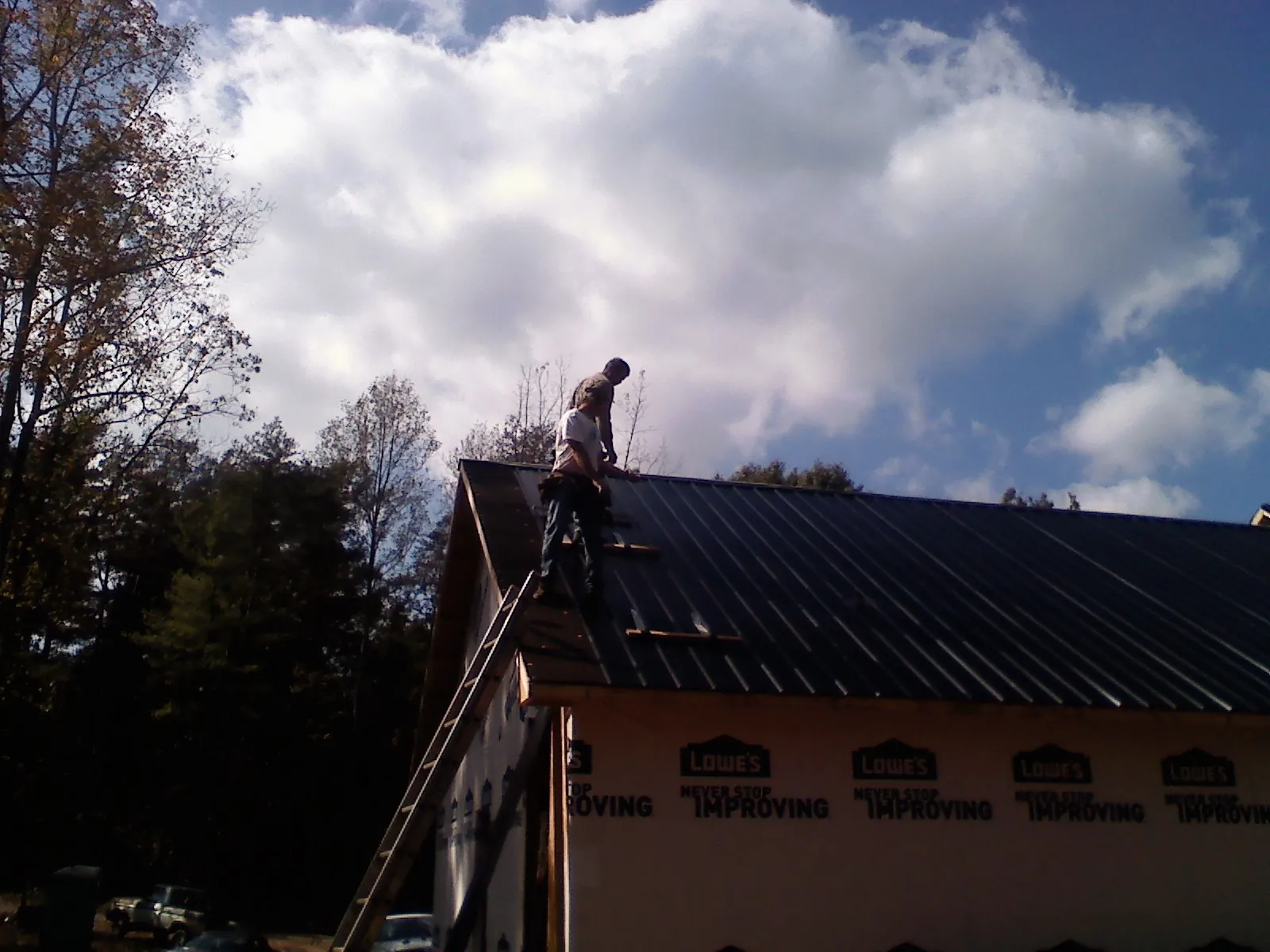 Roofer fastening dark metal panels high against a cloudy sky, from a Roof Inspection job in Atwood